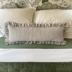 May include: A white bed with a green headboard featuring a floral pattern. Two white pillows and a black and white striped pillow with a ruffled edge are on the bed. The bed is covered with a white duvet and a green quilted bedspread.