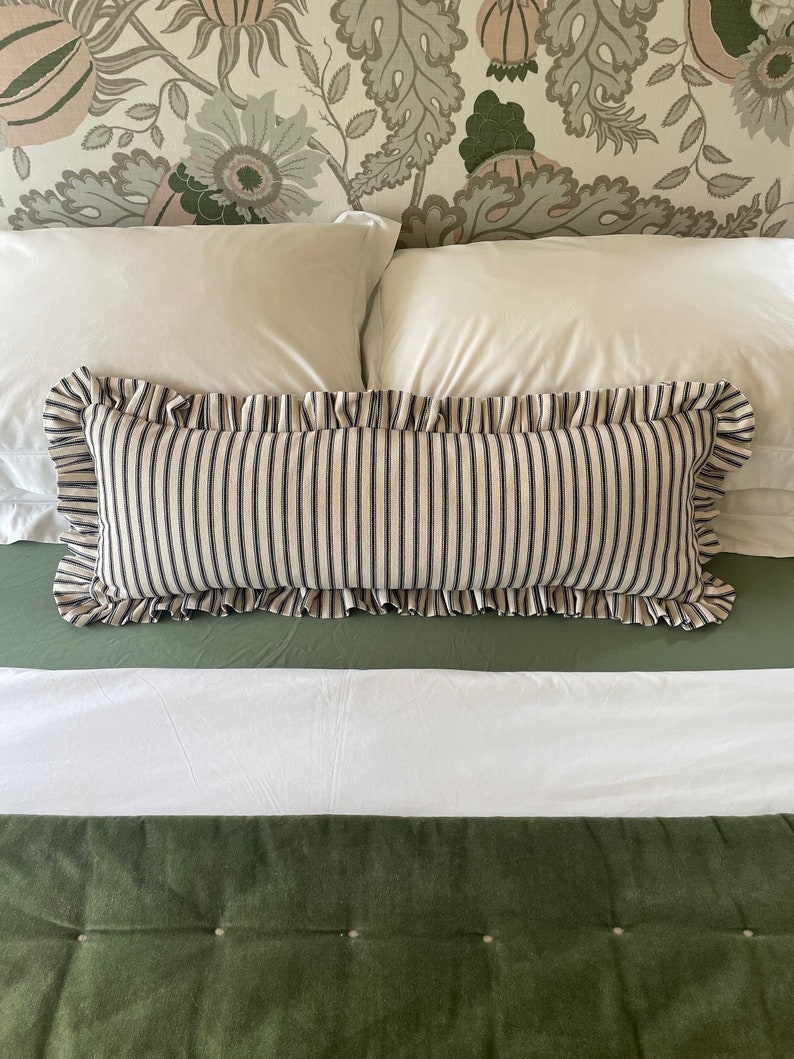 May include: A white bed with a green headboard featuring a floral pattern. Two white pillows and a black and white striped pillow with a ruffled edge are on the bed. The bed is covered with a white duvet and a green quilted bedspread.