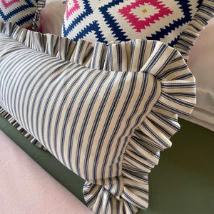 A navy ticking striped lumbar pillow on a bed with geometric pink and blue frilled cushions.