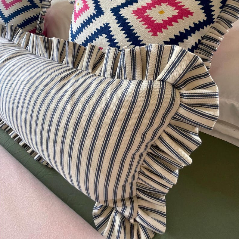 A navy ticking striped lumbar pillow on a bed with geometric pink and blue frilled cushions.