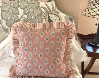 May include: A square throw pillow featuring a dusty pink fabric with a repeating pattern of small blue and white teardrop shapes. The pillow is bordered by a wide, gathered ruffle made of a pink and white striped fabric on all four sides.