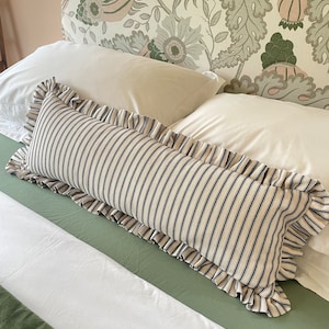 A white bed with a green headboard featuring a floral pattern. Two white pillows and a black and white striped pillow with a ruffled edge are on the bed. The bed is covered with a white duvet and a green quilted bedspread.