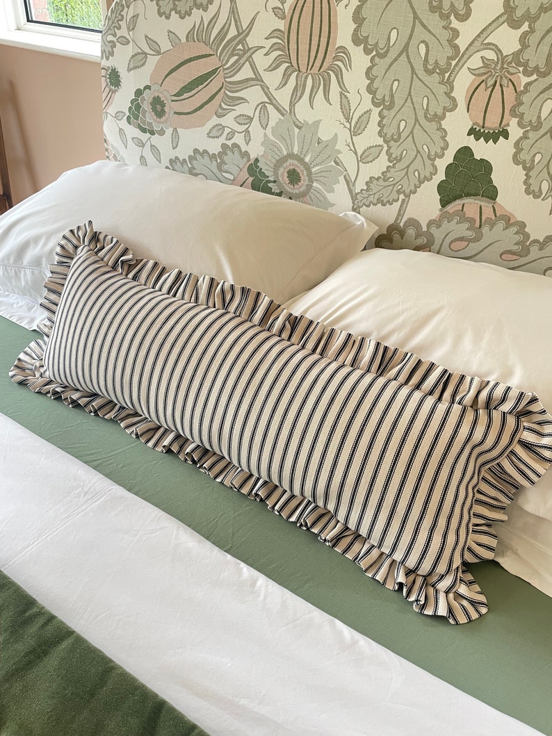 A white bed with a green headboard featuring a floral pattern. Two white pillows and a black and white striped pillow with a ruffled edge are on the bed. The bed is covered with a white duvet and a green quilted bedspread.