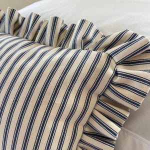 A detailed image of a navy and white ruffled lumbar pillow on a bed with white bedding