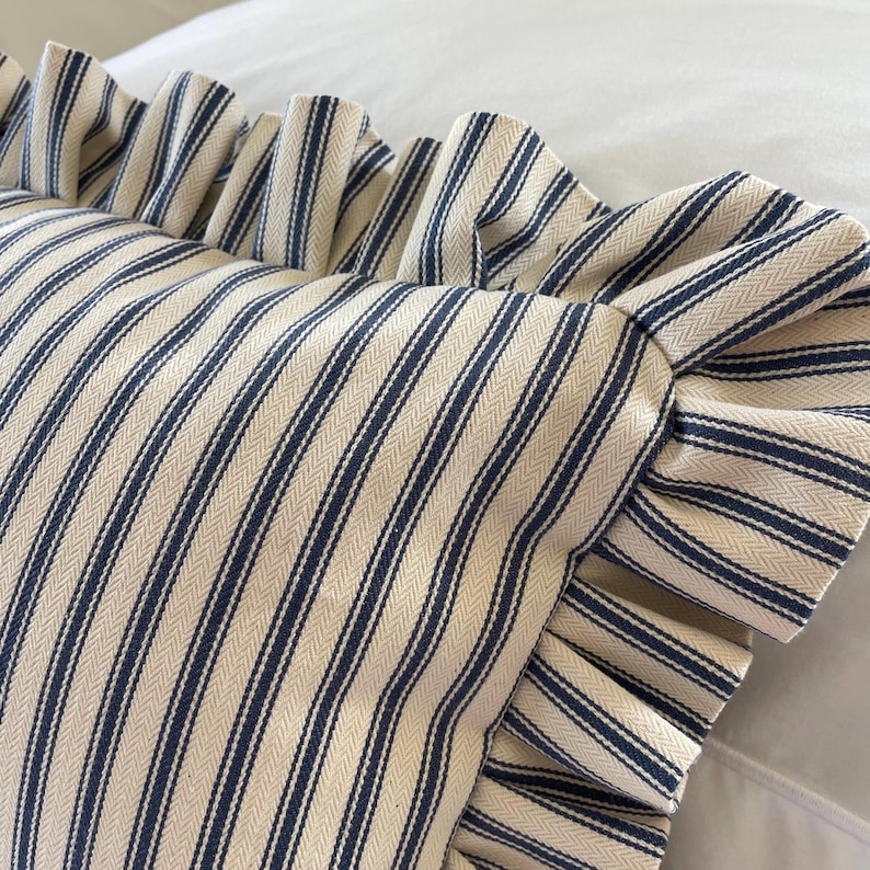 A detailed image of a navy and white ruffled lumbar pillow on a bed with white bedding