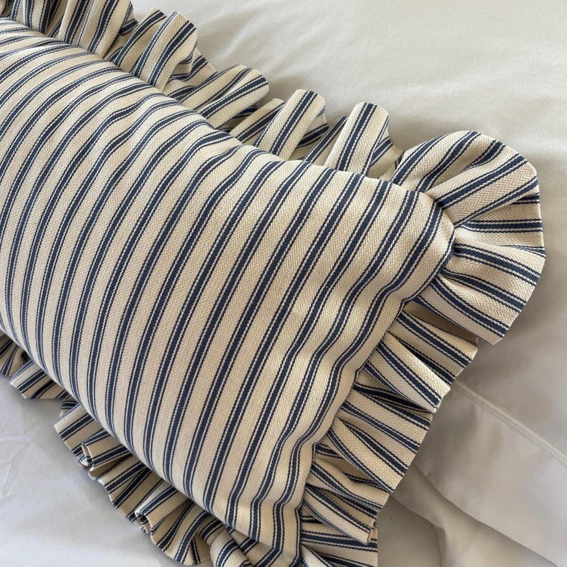A navy blue and white striped lumbar cushion with a ruffled edge sitting on a white bedding