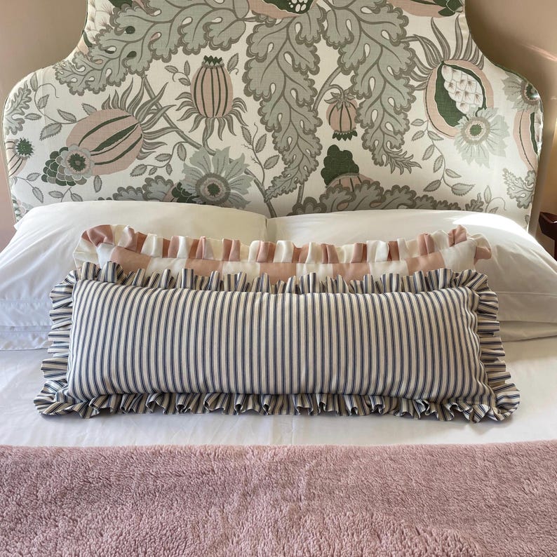 Navy and pink striped lumbar cushions sitting atop a bed with a pink bedspread and a floral headboard
