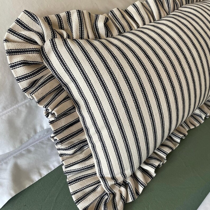 A black and white striped pillow with a ruffled edge. The pillow is on a green surface.