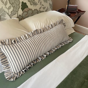 A white bed with a green headboard featuring a floral pattern. Two white pillows and a black and white striped pillow with a ruffled edge are on the bed. The bed is covered with a white duvet and a green quilted bedspread.