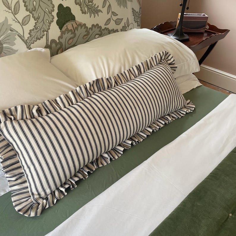 A white bed with a green headboard featuring a floral pattern. Two white pillows and a black and white striped pillow with a ruffled edge are on the bed. The bed is covered with a white duvet and a green quilted bedspread.
