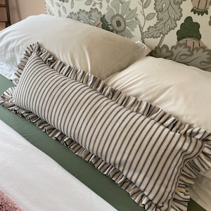 May include: A black and white striped pillow with a ruffled edge. The pillow is on a white bed with a green headboard.