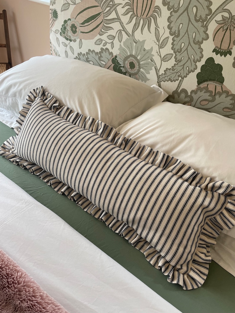May include: A black and white striped pillow with a ruffled edge. The pillow is on a white bed with a green headboard.