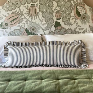 A white and green patterned headboard with a ruffled, navy striped lumbar pillow on a bed with a green quilted bedspread.