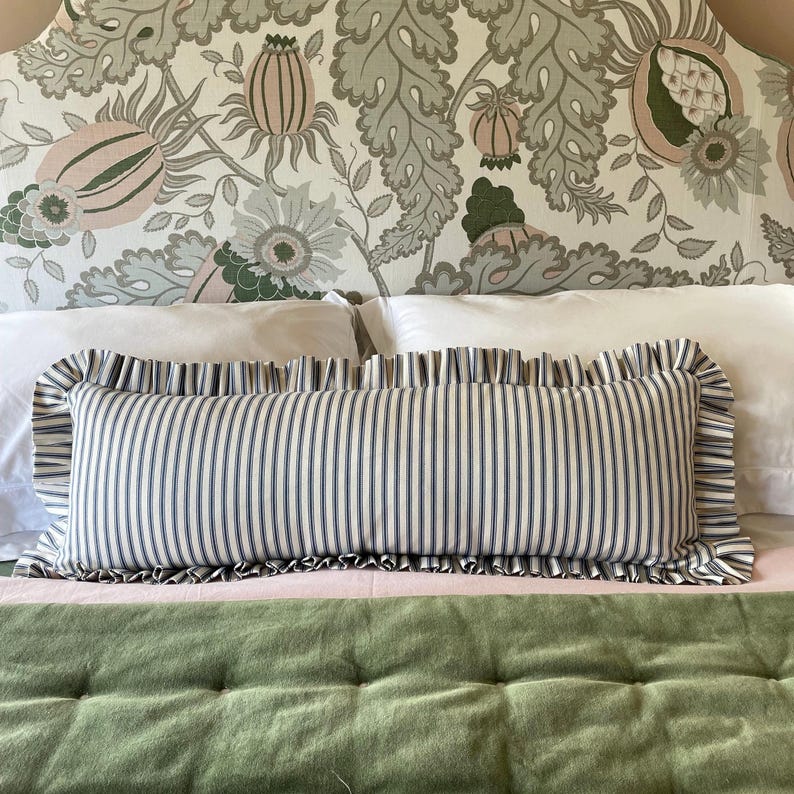 A white and green patterned headboard with a ruffled, navy striped lumbar pillow on a bed with a green quilted bedspread.