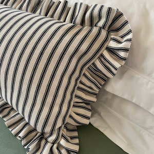 May include: A white pillow with black stripes and a ruffled edge. The pillow is on a white bed with a green sheet.