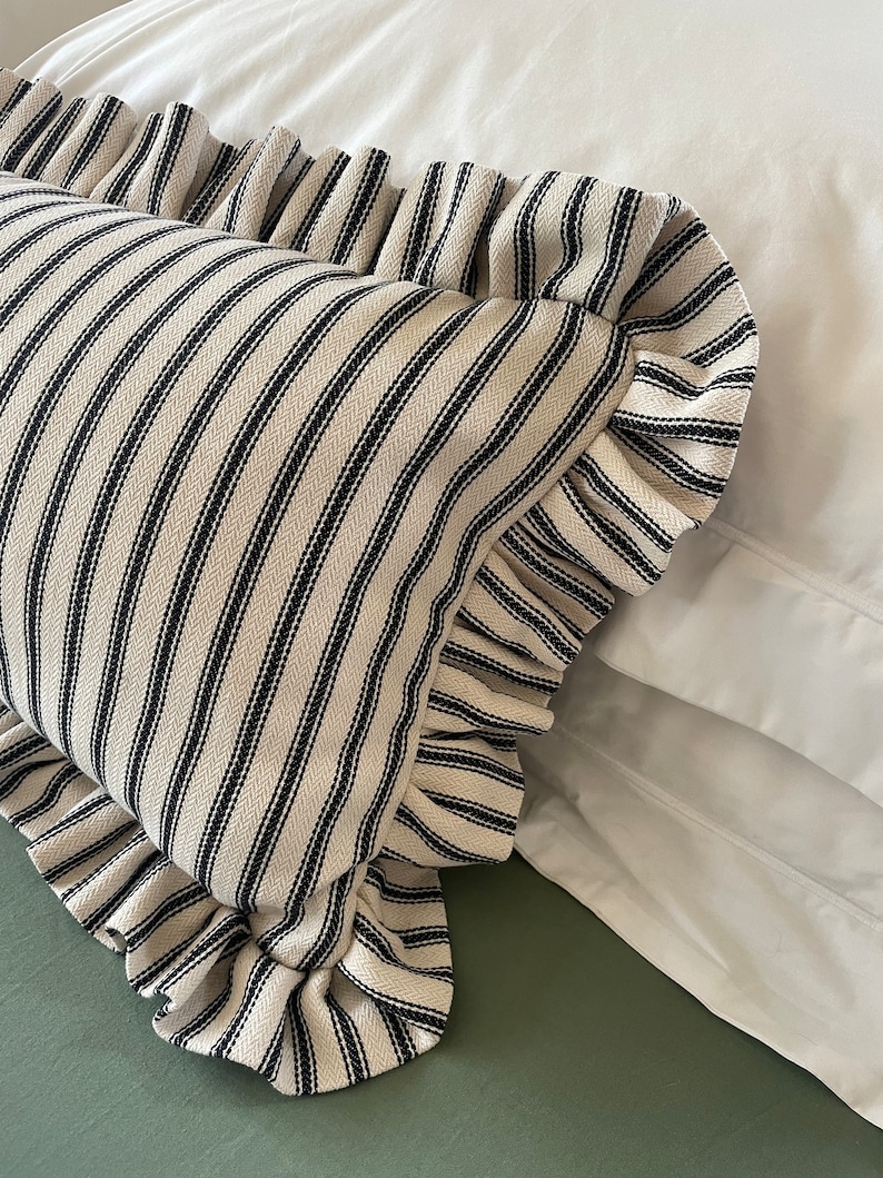 May include: A white pillow with black stripes and a ruffled edge. The pillow is on a white bed with a green sheet.