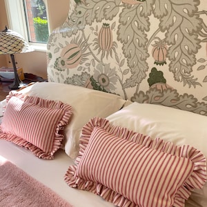 May include: Two white pillowcases with red and white striped pillow covers with ruffled edges. The pillows are on a bed with a floral patterned headboard.