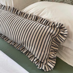 A white bed with a green headboard featuring a floral pattern. Two white pillows and a black and white striped pillow with a ruffled edge are on the bed. The bed is covered with a white duvet and a green quilted bedspread.