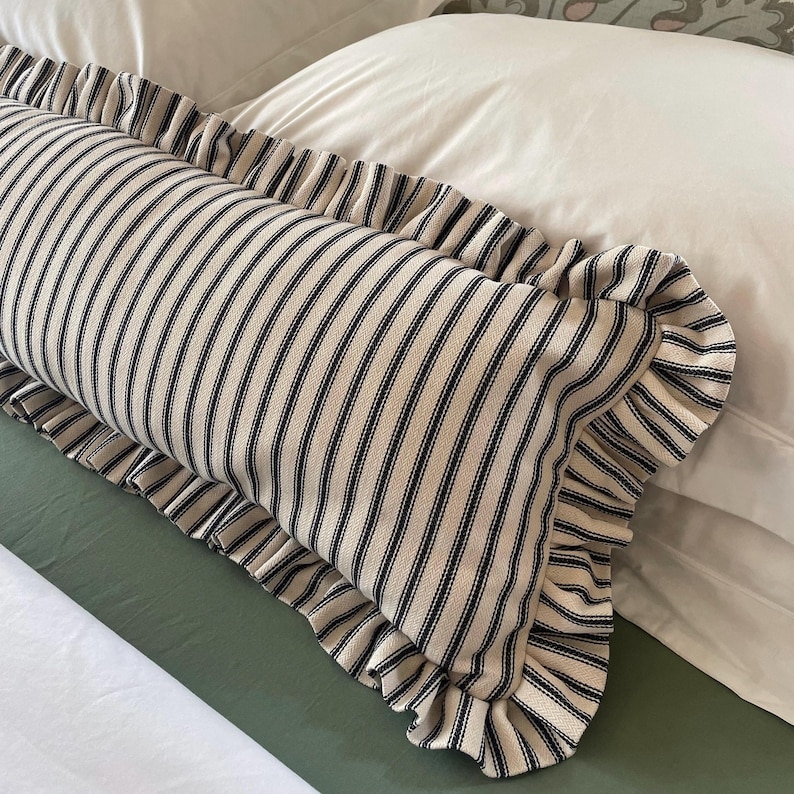 A white bed with a green headboard featuring a floral pattern. Two white pillows and a black and white striped pillow with a ruffled edge are on the bed. The bed is covered with a white duvet and a green quilted bedspread.
