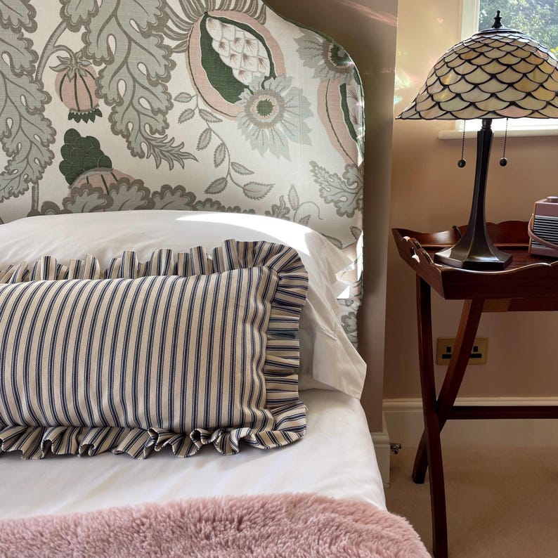 Navy and white striped lumbar cushions sitting on a bed with a large floral headboard and a pink bedspread