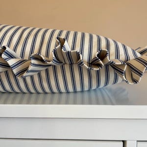 A navy blue and white striped lumbar cushion with matching ruffled trim sitting atop a white chest of drawers
