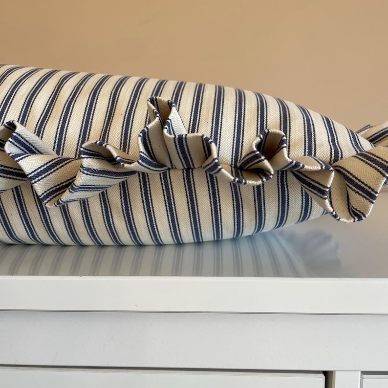 A navy blue and white striped lumbar cushion with matching ruffled trim sitting atop a white chest of drawers