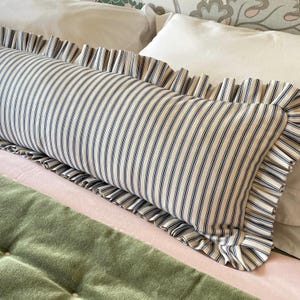 A striped lumbar pillow with ruffle in navy blue cotton ticking on a bed with a green quilted bedspread.