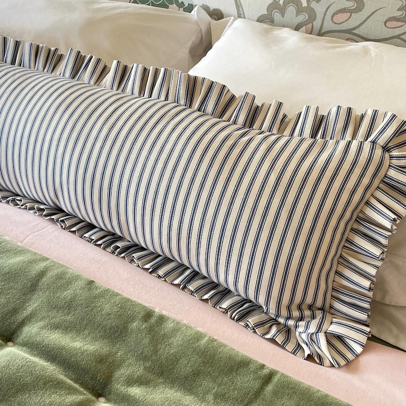 A striped lumbar pillow with ruffle in navy blue cotton ticking on a bed with a green quilted bedspread.