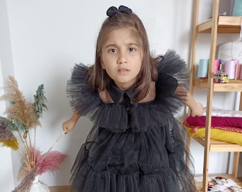 Könnte beinhalten: Ein junges Mädchen trägt ein schwarzes Tüllkleid mit einem Rüschenkragen und einer schwarzen Schleife im Haar.