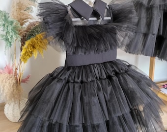 Könnte beinhalten: Ein schwarzes Tüllkleid mit einem gestuften Rock und einem eng anliegenden Oberteil. Das Kleid hat einen Peter Pan-Kragen und kurze Ärmel. Das Kleid wird auf einer Schaufensterpuppe und einem Kleiderbügel präsentiert.