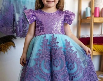 May include: A dress featuring a purple sequined bodice with short sleeves and a light blue tulle skirt. The skirt is adorned with intricate purple lace embroidery in a circular pattern. A matching purple butterfly hair accessory is included.