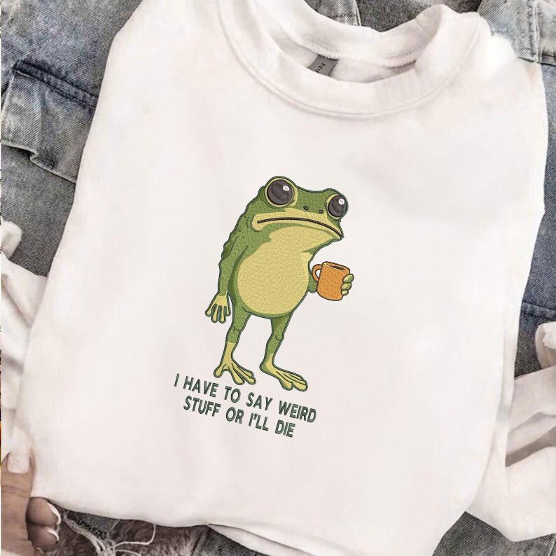Peut inclure: Sweat-shirt blanc avec une grenouille de dessin anim&eacute; tenant une tasse. La grenouille est verte et jaune avec de grands yeux. Le texte en dessous de la grenouille dit : "I HAVE TO SAY WEIRD STUFF OR I'LL DIE."