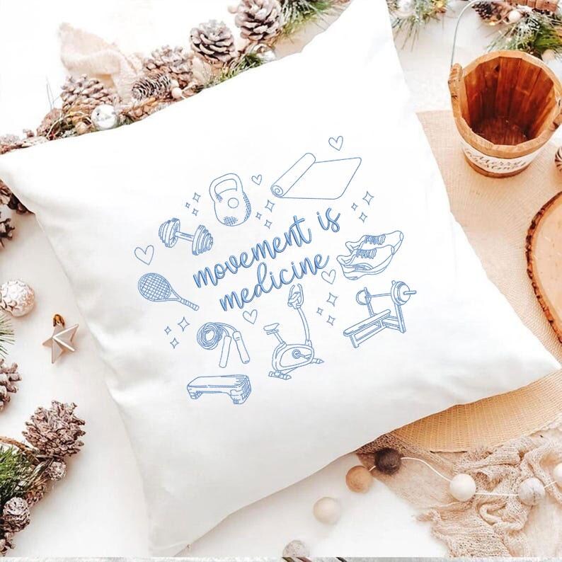 May include: White square pillow with a blue line drawing of fitness equipment and the words "movement is medicine." The design includes a dumbbell, kettlebell, yoga mat, tennis racket, and exercise bike.