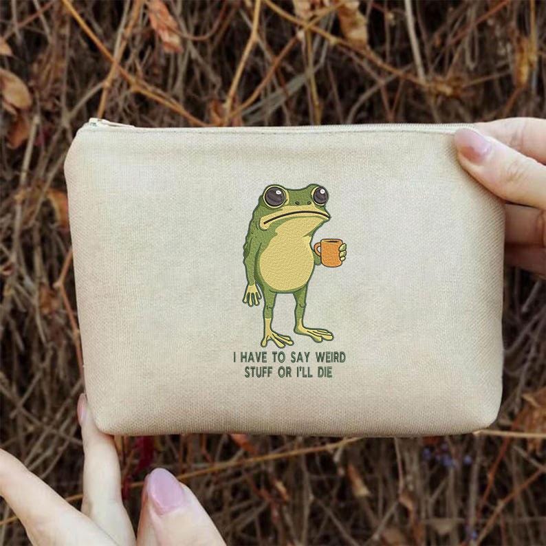 Peut inclure: Pochette en toile beige avec une illustration de grenouille verte tenant une tasse orange. La grenouille a de grands yeux et une expression d&eacute;tendue. Le texte en dessous dit : "I HAVE TO SAY WEIRD STUFF OR I'LL DIE."