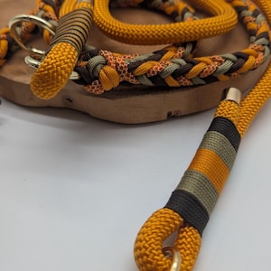 May include: A dog leash and collar set in shades of yellow, brown, and green. The leash is made of thick, braided rope with gold-colored metal hardware. The collar features a similar design with a matching color scheme.