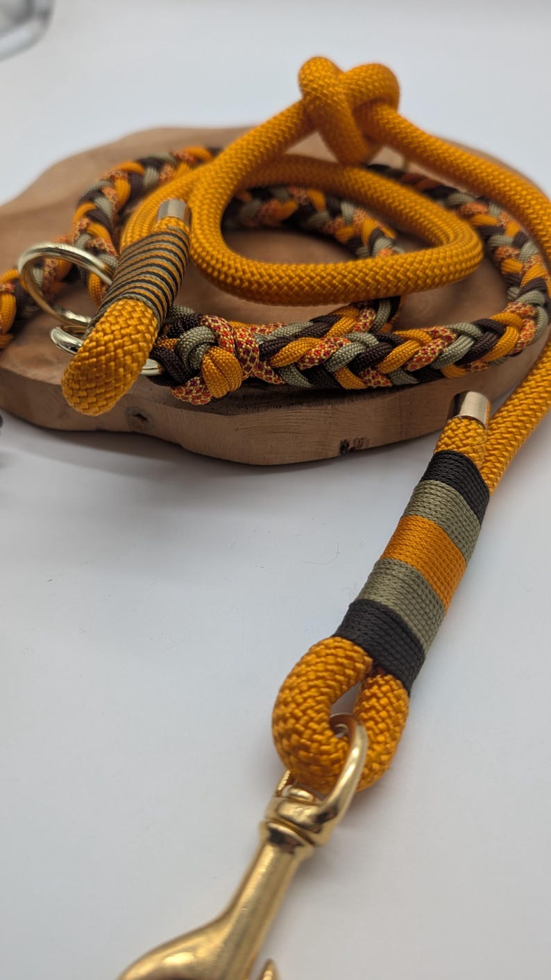 May include: A dog leash and collar set in shades of yellow, brown, and green. The leash is made of thick, braided rope with gold-colored metal hardware. The collar features a similar design with a matching color scheme.