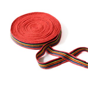 May include: A roll of red and multi-colored striped ribbon. The ribbon is coiled and has a rainbow stripe pattern.