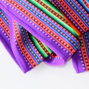 Puede incluir: Una tela morada con rayas de colores y patrones geométricos. La tela está doblada por la mitad y los bordes son visibles.