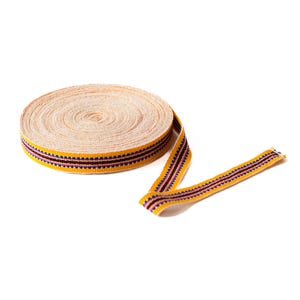 May include: A roll of yellow and purple striped ribbon with a white background. The ribbon is rolled up and a portion of it is unrolled.