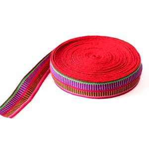 Puede incluir: Un rollo de cinta roja con un patrón de rayas multicolores. La cinta está enrollada en un círculo y tiene un extremo suelto.