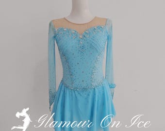 May include: A light blue figure skating costume with long sleeves and a sheer neckline. The bodice is embellished with sparkling crystals and the skirt is a flared design. The text "Glamour On Ice" and "Figure Skating Costume by Chloe" are visible.