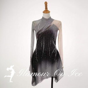 Könnte beinhalten: Ein langärmeliges Eiskunstlaufkleid mit einem Farbverlauf von Hellgrau zu Schwarz. Das Oberteil und die Ärmel sind mit verstreuten klaren Kristallen besetzt, und der Rock hat einen asymmetrischen Saum mit transparenten Stofflagen.