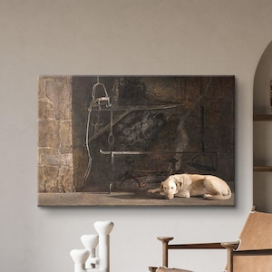 May include: A framed canvas art print depicting a dog lying down in front of a dark, industrial background. The artwork is displayed above a wooden side table with white decorative objects and a leather chair.