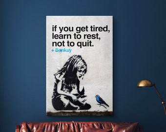 May include: A black and white stencil print of a girl sitting with a bird on a white background. The print has the quote "if you get tired, learn to rest, not to quit." and the signature "Banksy".