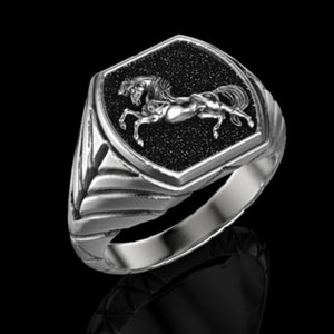 Puede incluir: Un anillo de plata con una piedra negra que presenta un diseño de caballo de plata detallado.