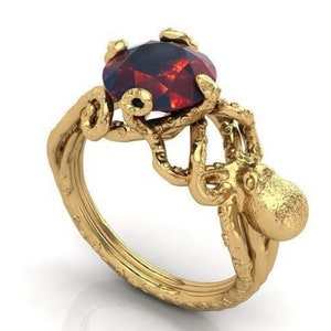 May include: A gold ring with an octopus design holding a red gemstone. The octopus is detailed with textured tentacles and a round body.