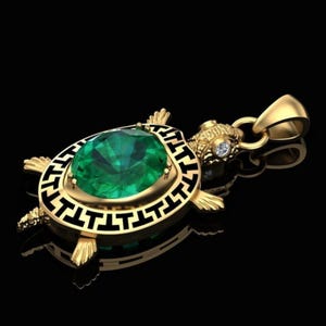 May include: A gold-colored turtle pendant with a large, faceted emerald-green gemstone at its center. The pendant has a black and gold Greek key design around the gemstone and a small diamond accent. The pendant is on a black background.