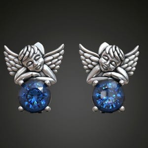 May include: A pair of silver earrings featuring a sleeping angel design with a blue gemstone in the center.