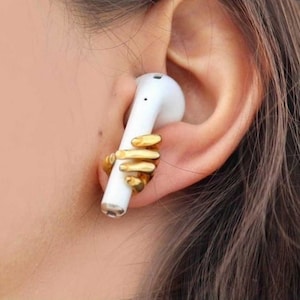 May include: A white wireless earbud with a gold hand-shaped accessory attached to it.