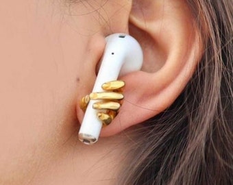 May include: A white wireless earbud with a gold hand-shaped accessory attached to it.